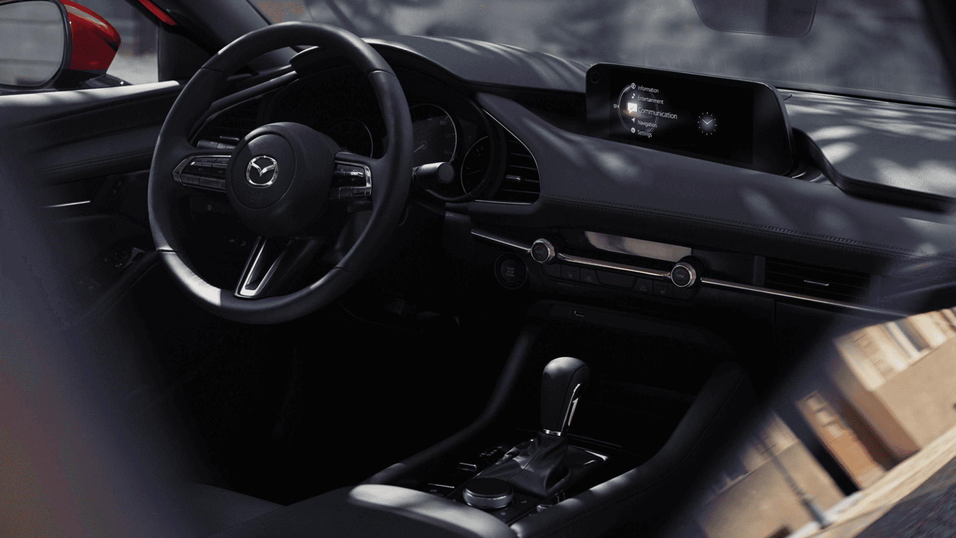 Interior view of Mazda3 cabin showing dashboard, steering wheel, center display, and gear shifter in low lighting