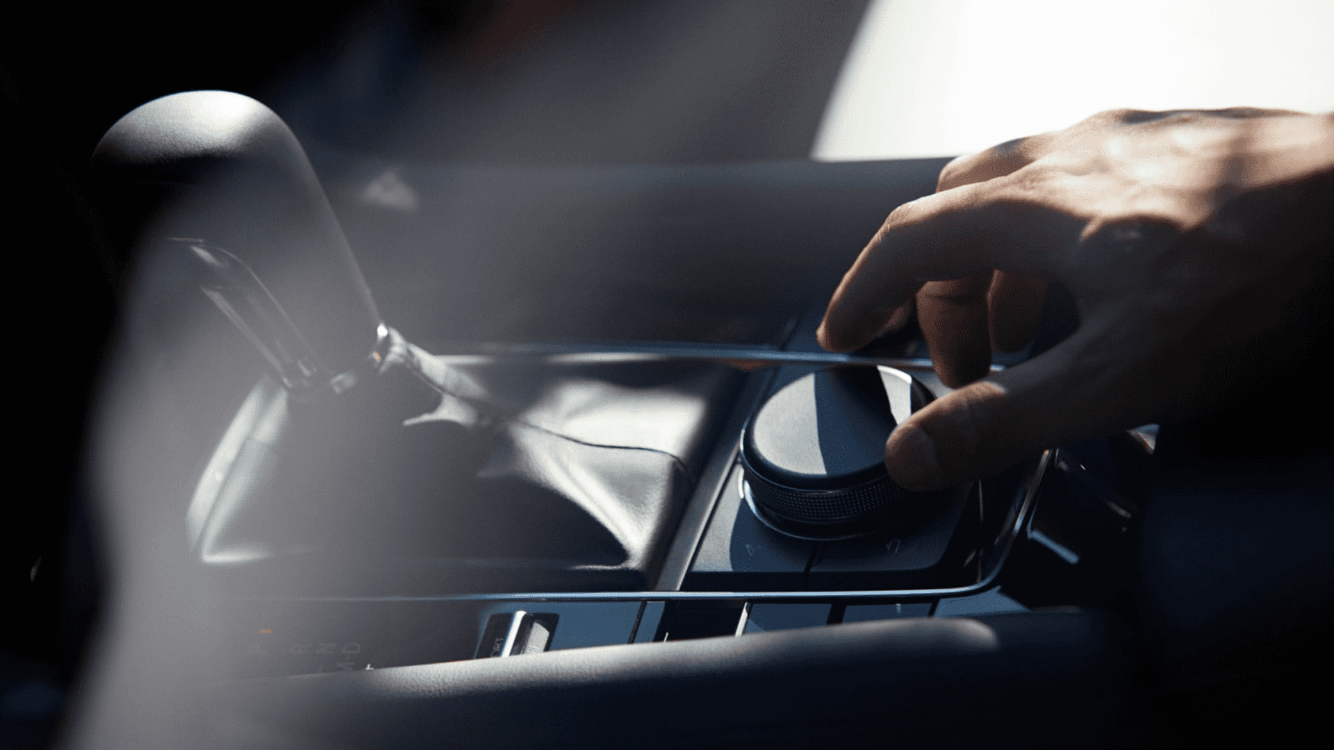 Hand adjusting rotary control knob near gear selector in Mazda3 center console with surrounding buttons visible
