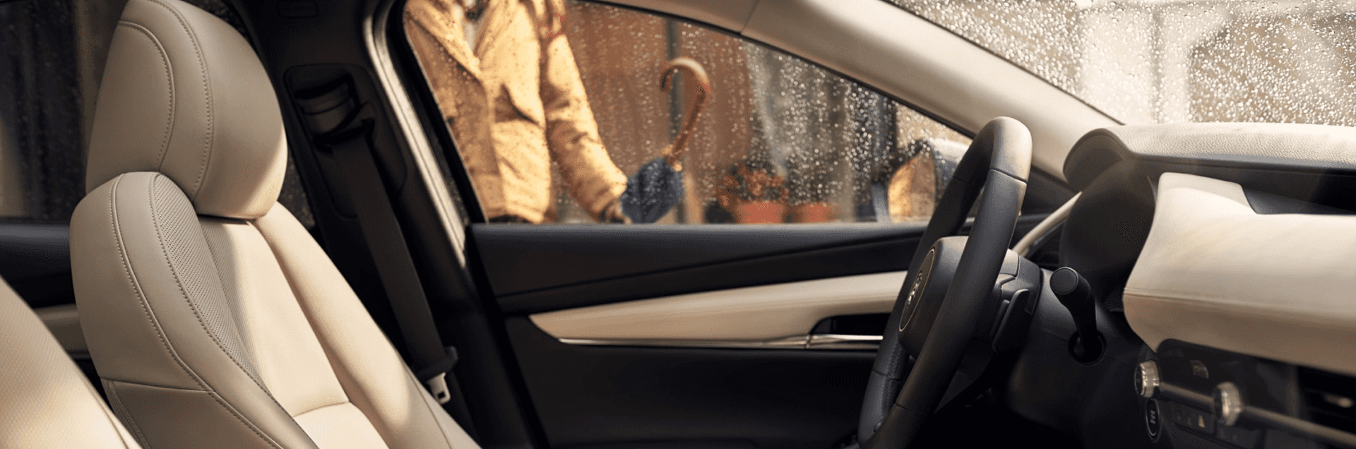 Front passenger seat in Mazda3 with light upholstery, dashboard, steering wheel, and rain visible through window