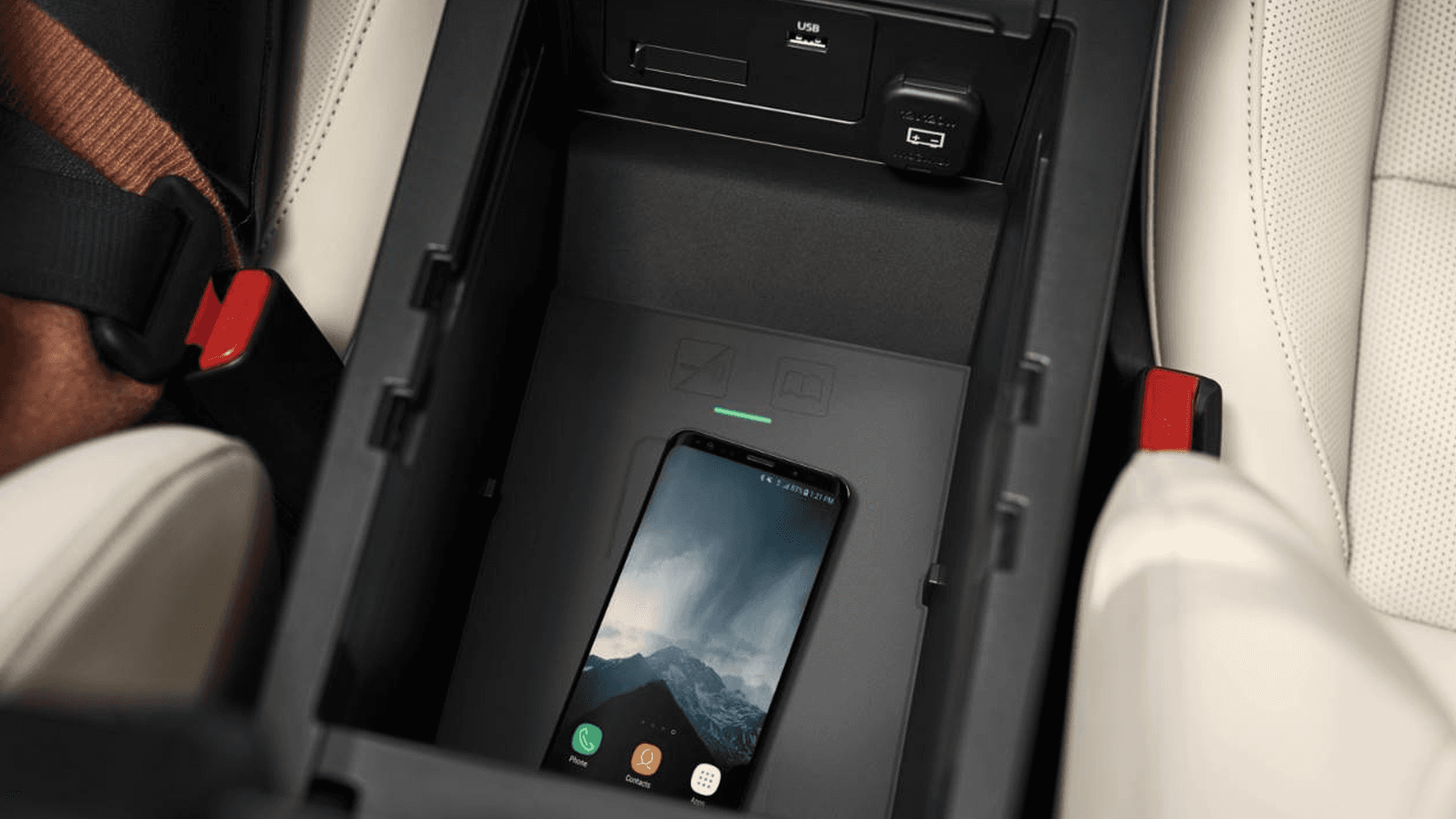 Open center console with wireless phone charging pad, USB port, power outlet, and smartphone resting inside.