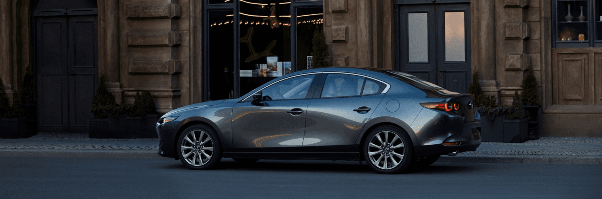 Gray hatchback parked on a concrete drive outside a modern building with tall white walls and dark garage doors