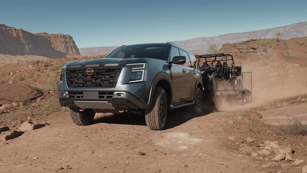 Green Nissan Armada towing a side-by-side vehicle on a trailer across a rocky desert landscape