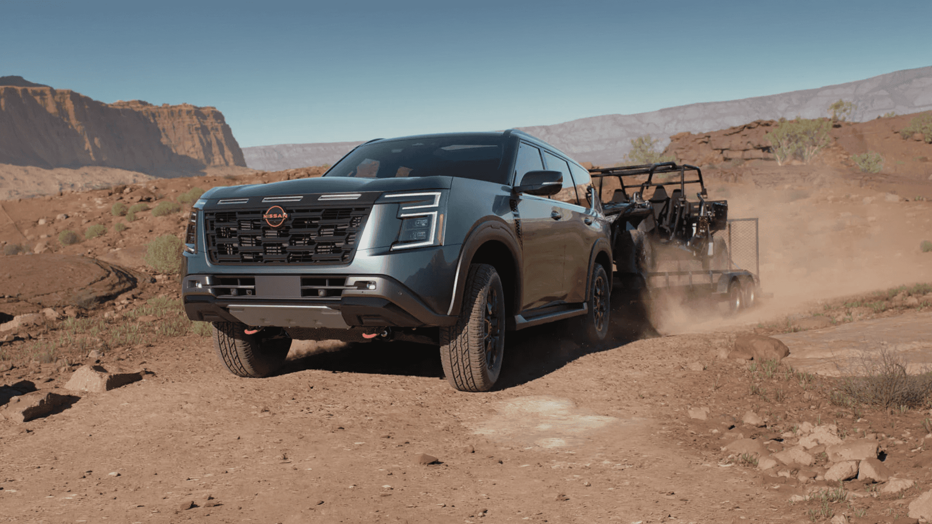 Green Nissan Armada driving over uneven rocky terrain with dust trailing behind in a wide desert landscape