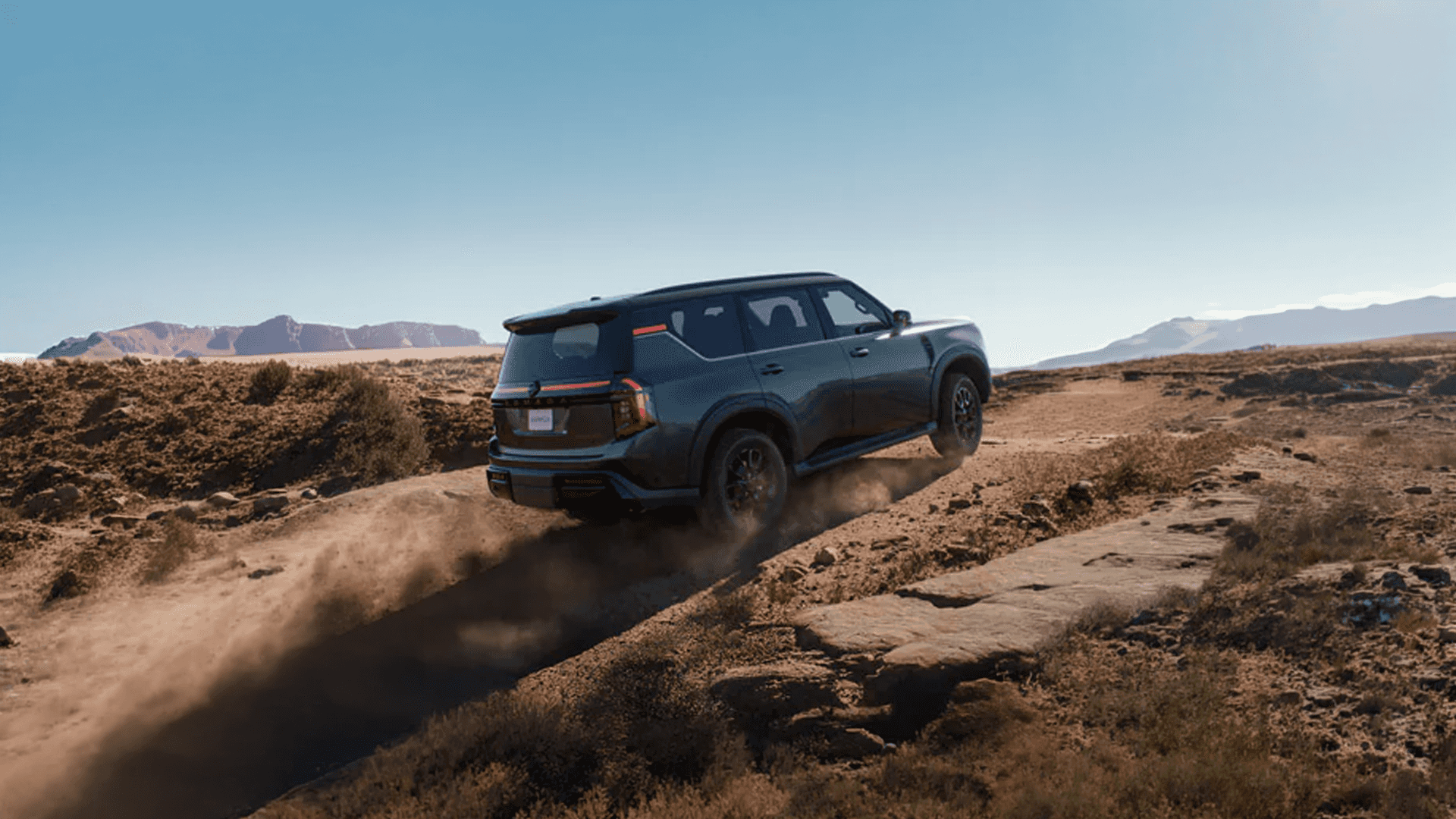 Green Nissan Armada driving over uneven rocky terrain with dust trailing behind in a wide desert landscape