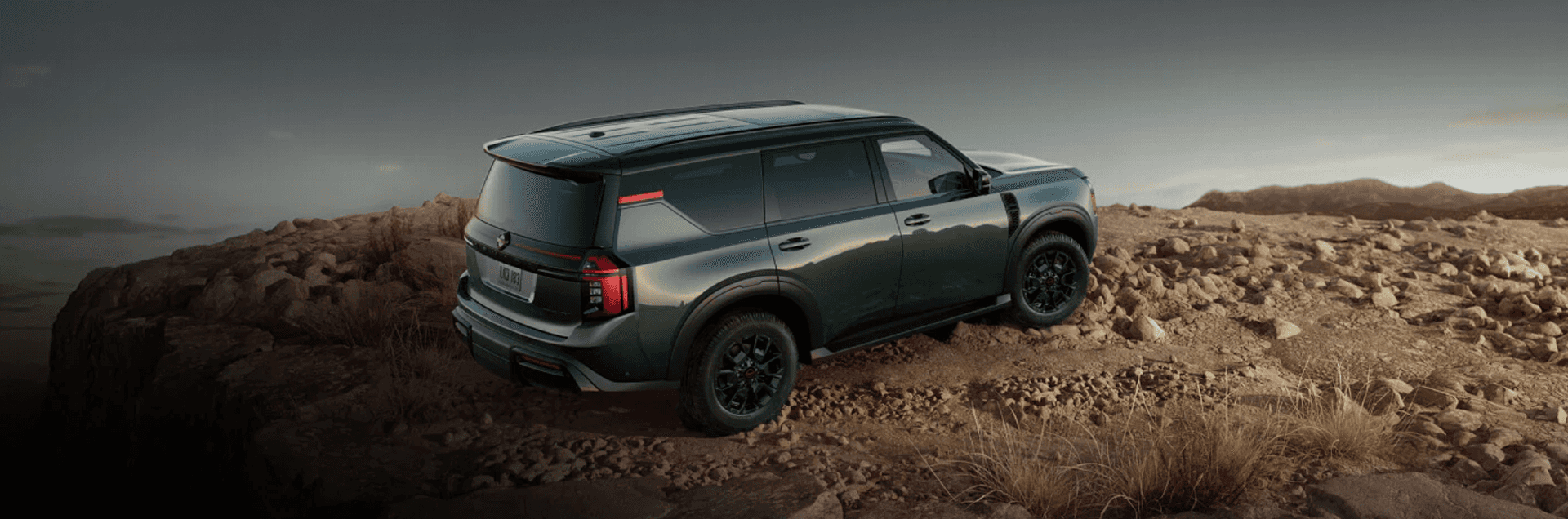 Green Nissan Armada parked on rocky terrain near a cliff edge with a rugged landscape and distant hills