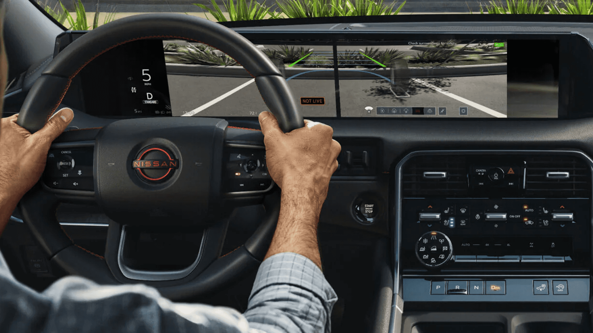 Driver holding steering wheel with digital dashboard display and center screen showing parking camera view