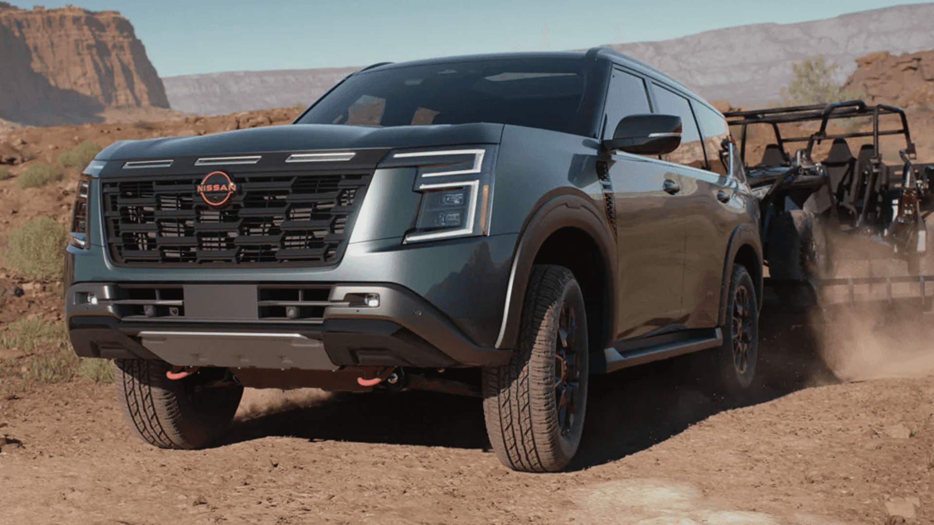 Green Nissan Armada driving on a dirt trail pulling an off road trailer through a rocky desert landscape