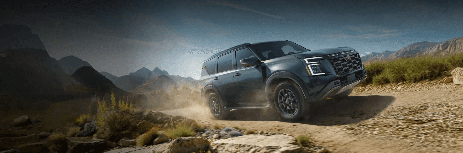 Green Nissan Armada driving on a dusty off road path surrounded by mountains and rugged terrain