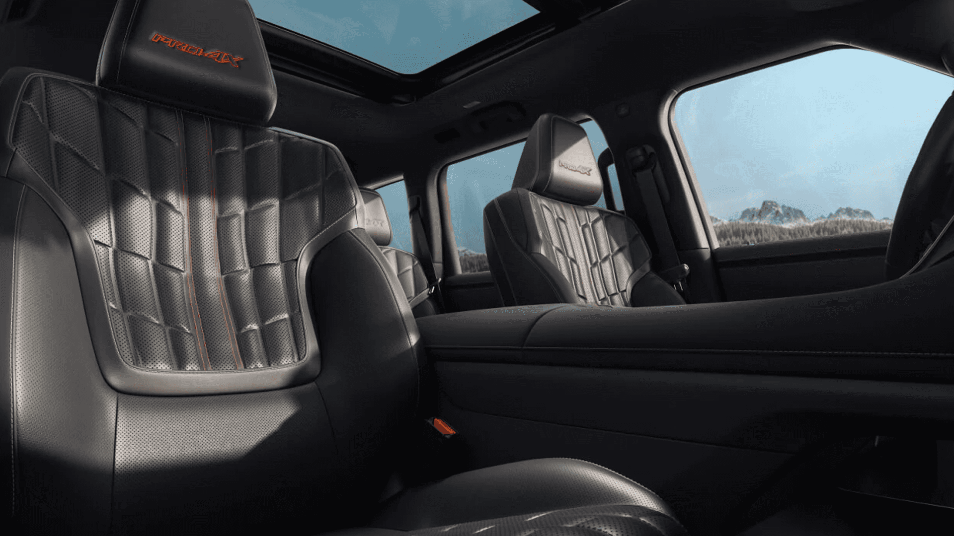 Black leather front seats with orange stitching, PRO-4X logos on headrests, and panoramic roof above