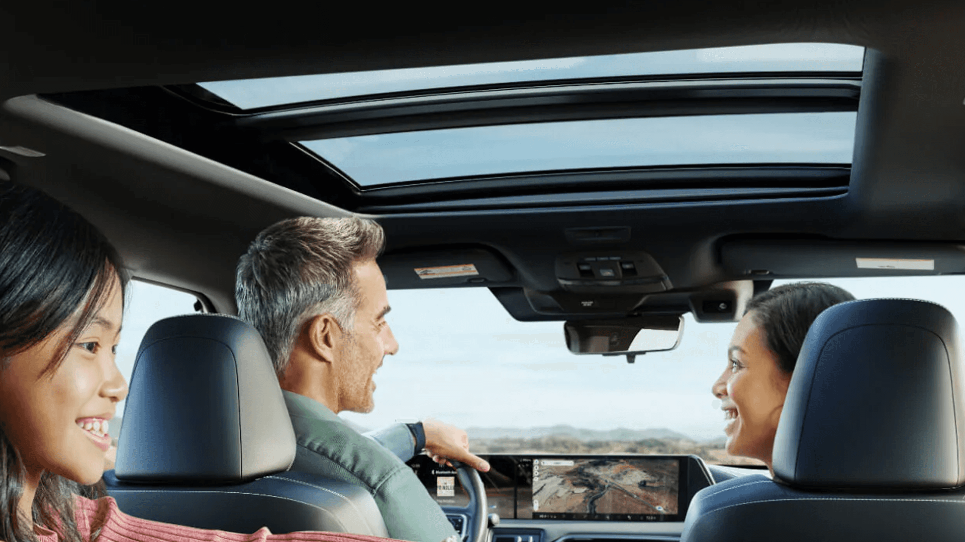 Interior view from rear seats showing panoramic glass roof with two passengers looking forward in cabin