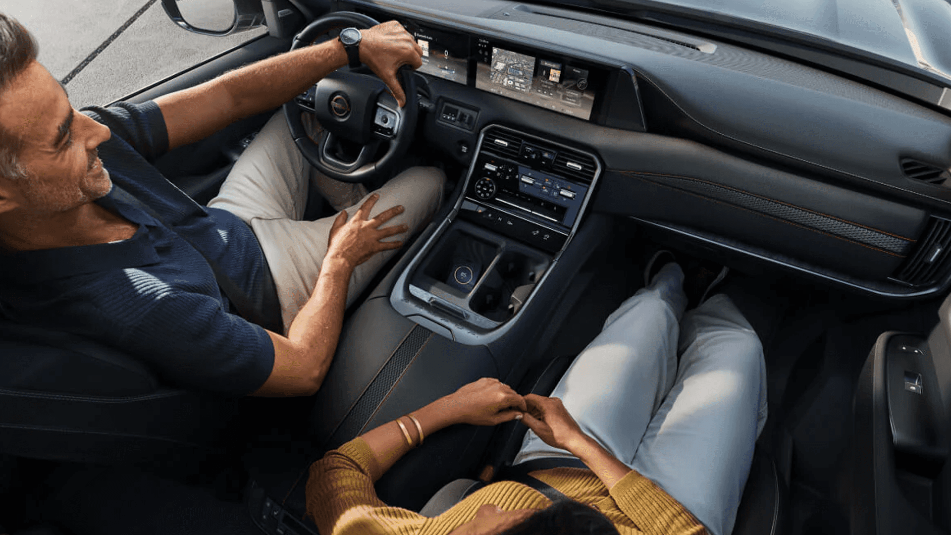 Overhead angle of dashboard showing wide dual displays, steering wheel, center console, and front seats