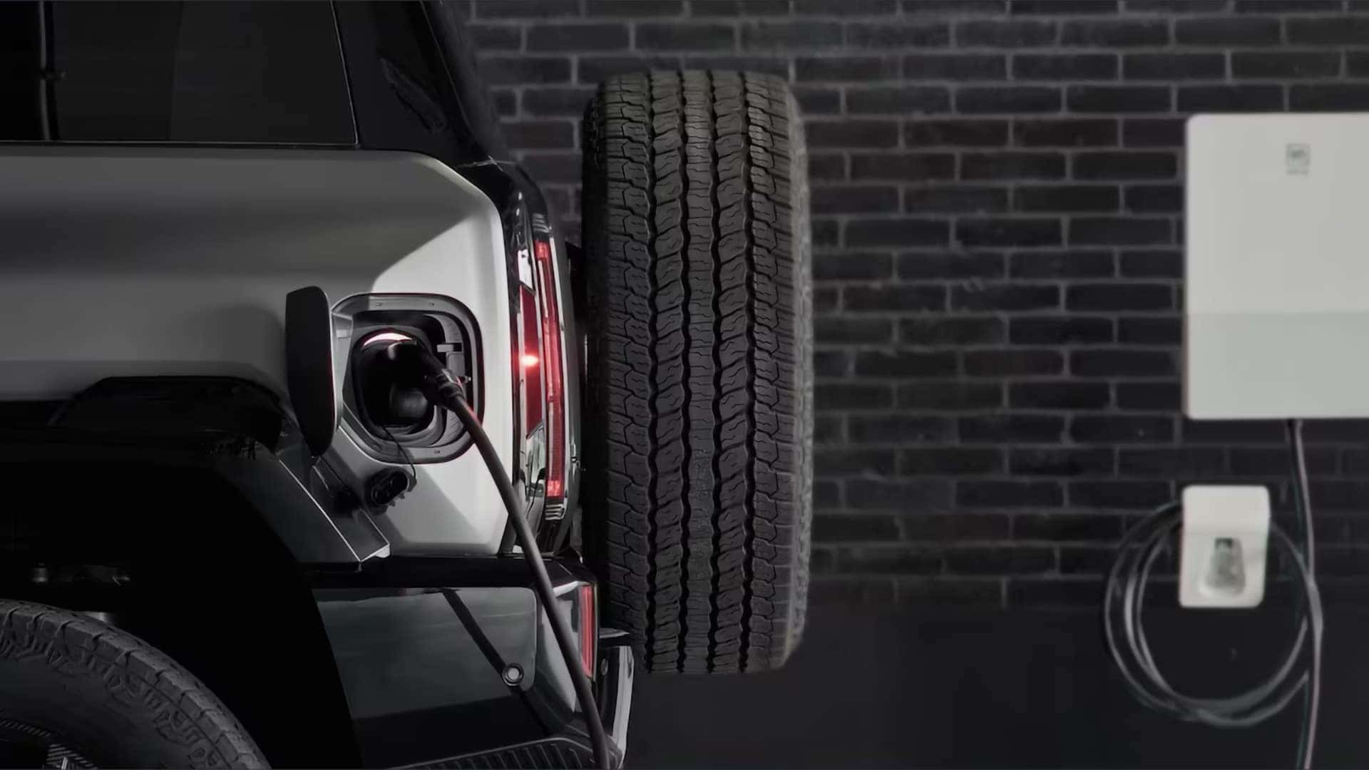 2026 GMC HUMMER EV SUV plugged into home charging station with rear mounted charge port