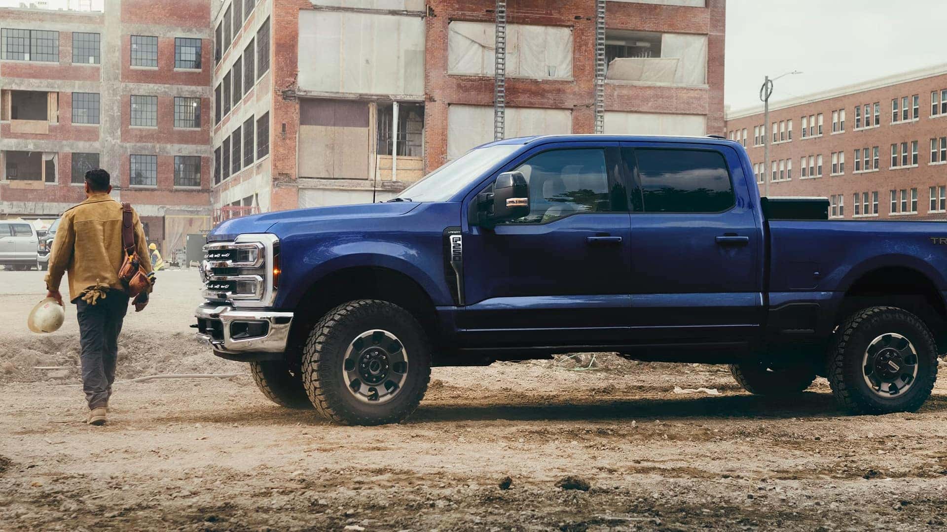 Side profile of blue 2026 Ford F-350 Super Duty at a construction site, showing long bed, crew cab, and work truck proportions