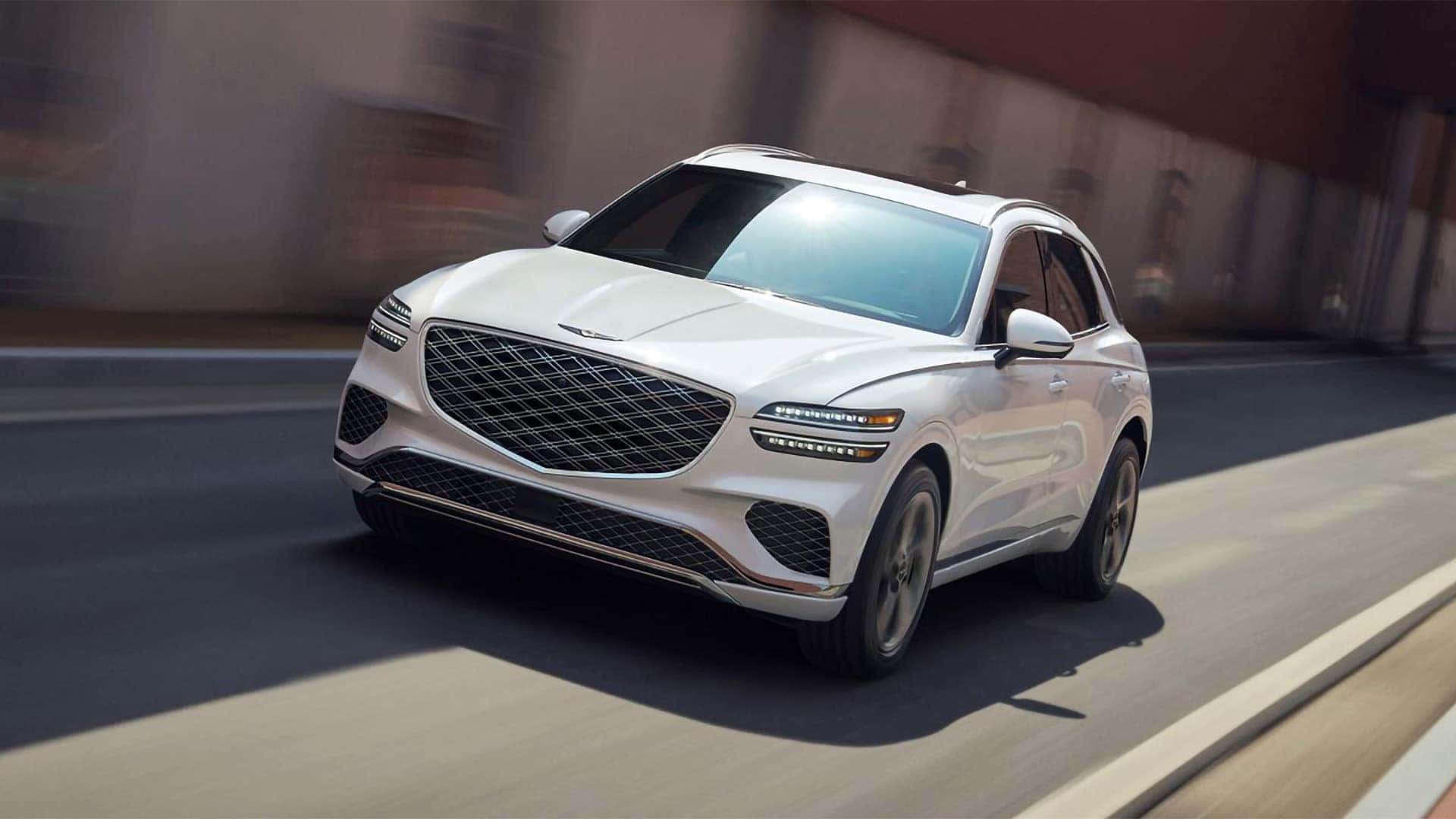 2026 Genesis GV70 driving on a city street, highlighting front grille design and smooth motion