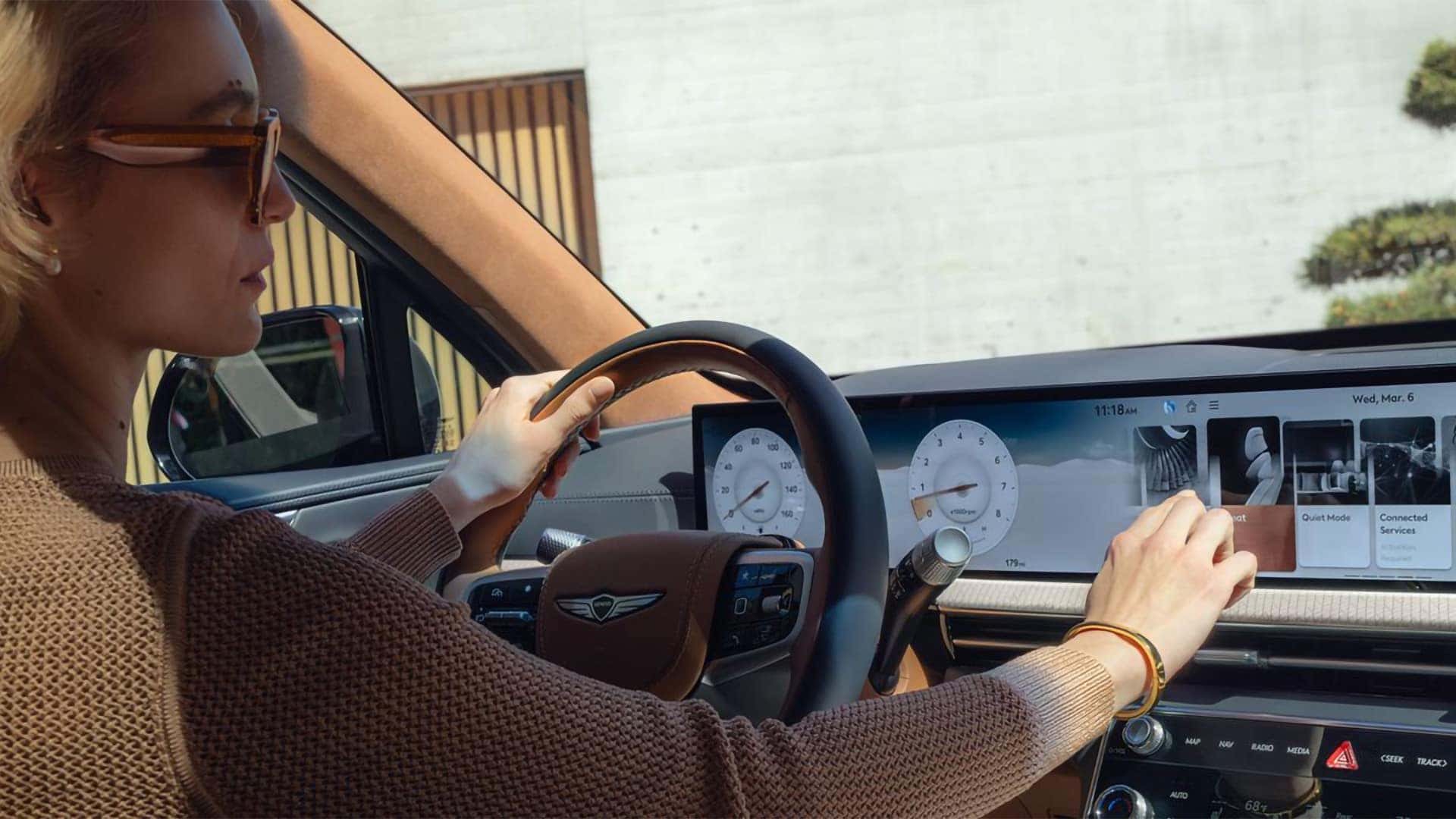 Driver using widescreen OLED display inside the 2026 Genesis GV80 showing digital gauges and infotainment controls