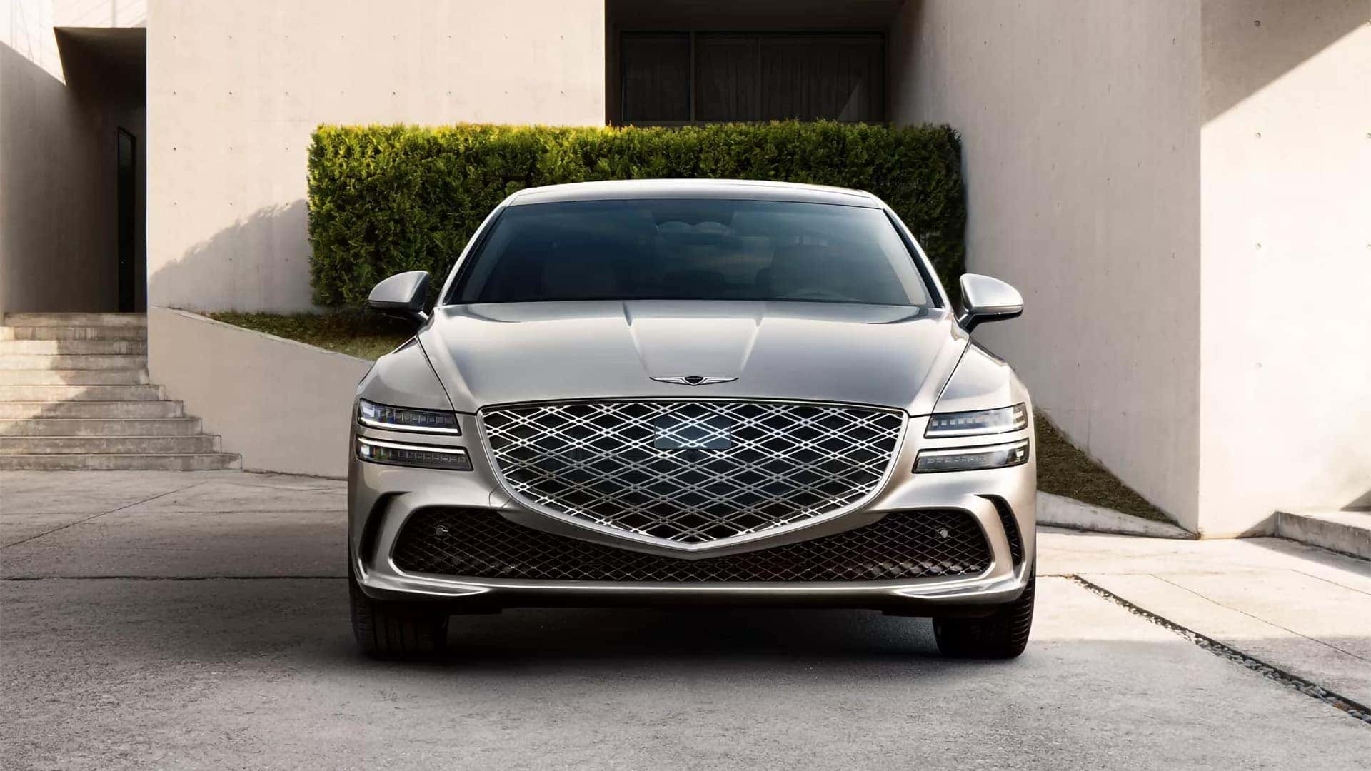 2026 Genesis G80 front view with crest grille and LED headlights in a luxury residential setting