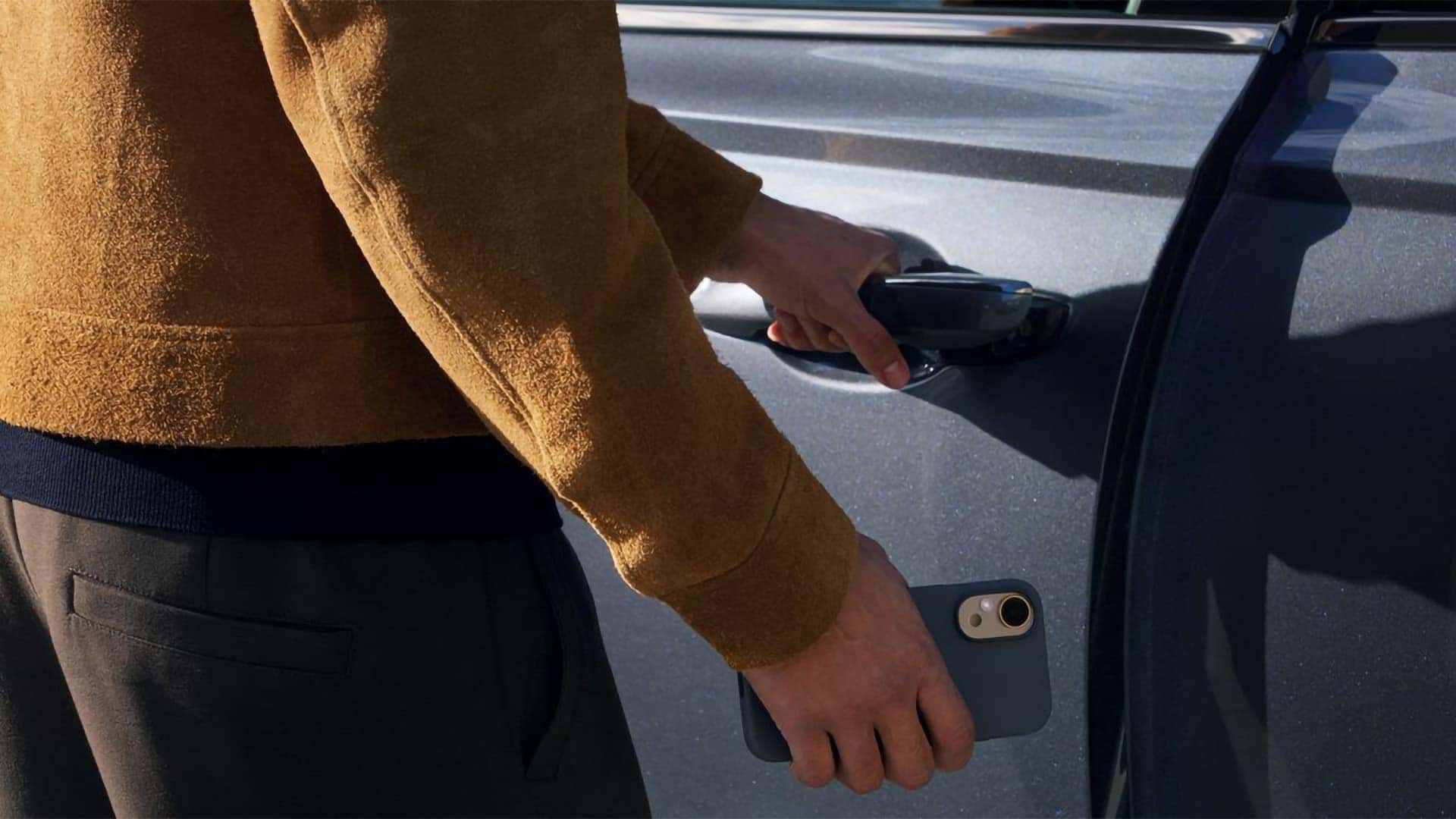 Person using smartphone near 2026 Genesis GV70 door handle demonstrating Digital Key exterior access feature