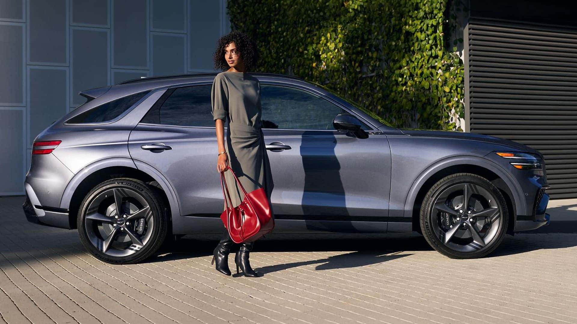 2026 Genesis GV70 parked near modern building with driver walking beside vehicle showcasing exterior design and proportions
