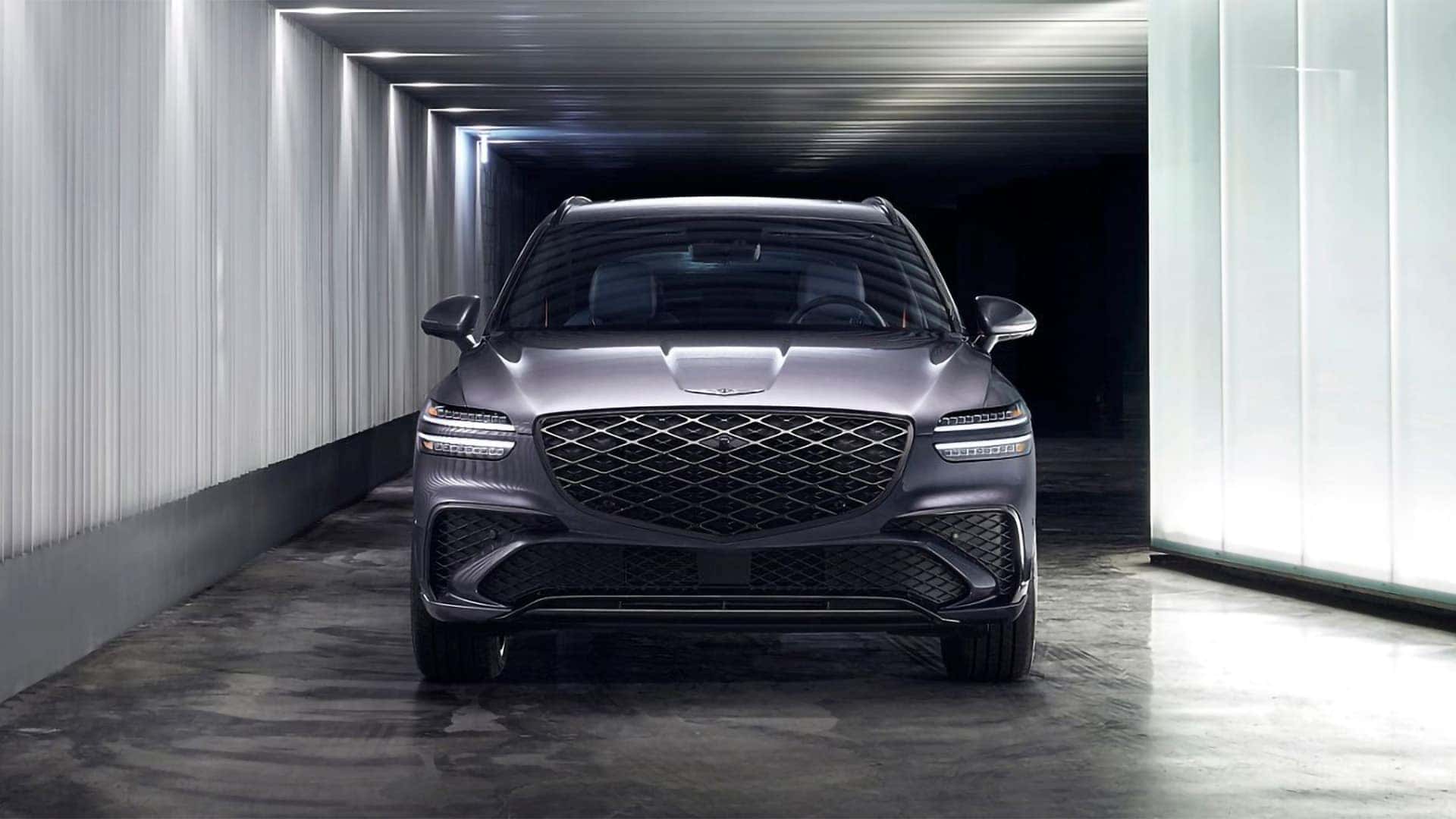 2026 Genesis GV70 front view in a modern garage setting, emphasizing grille design and LED lighting