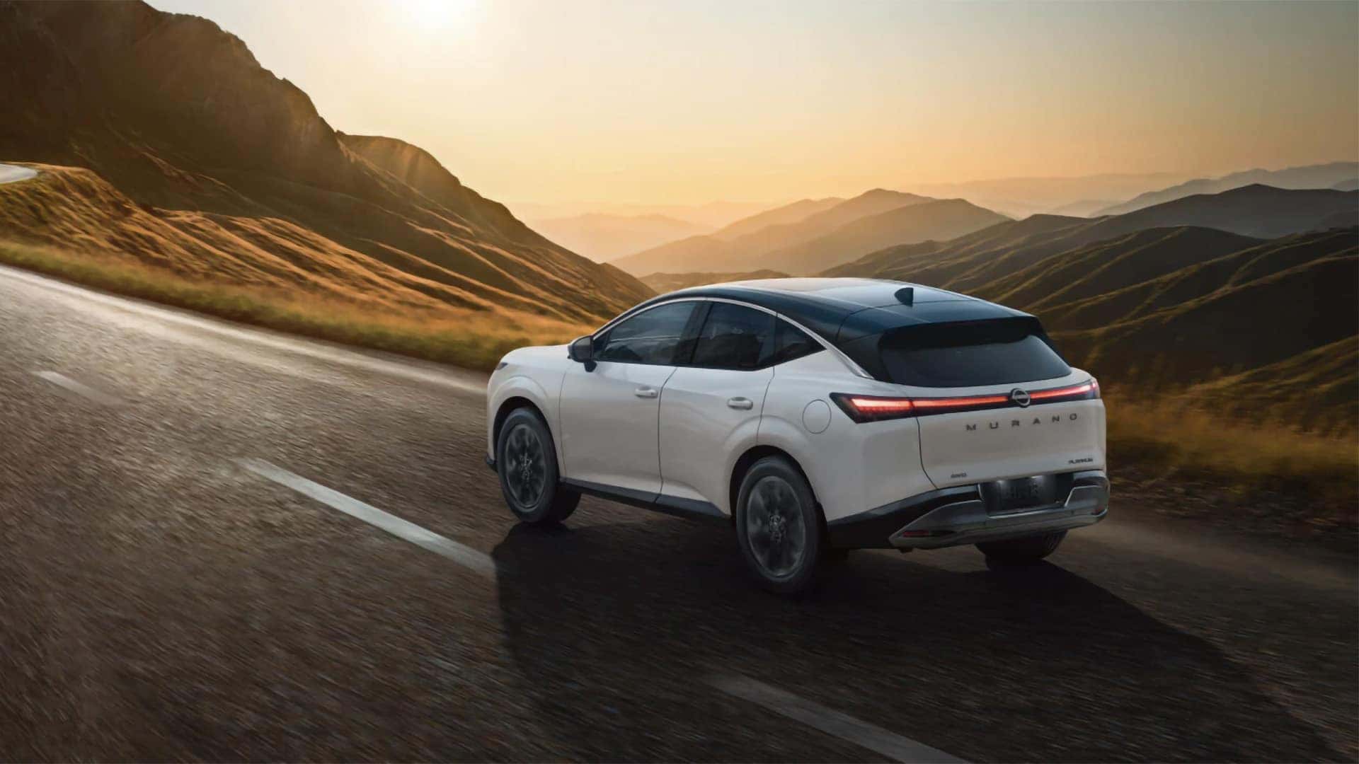 2026 Nissan Murano driving on a mountain road at sunset, rear view showing LED taillights and design