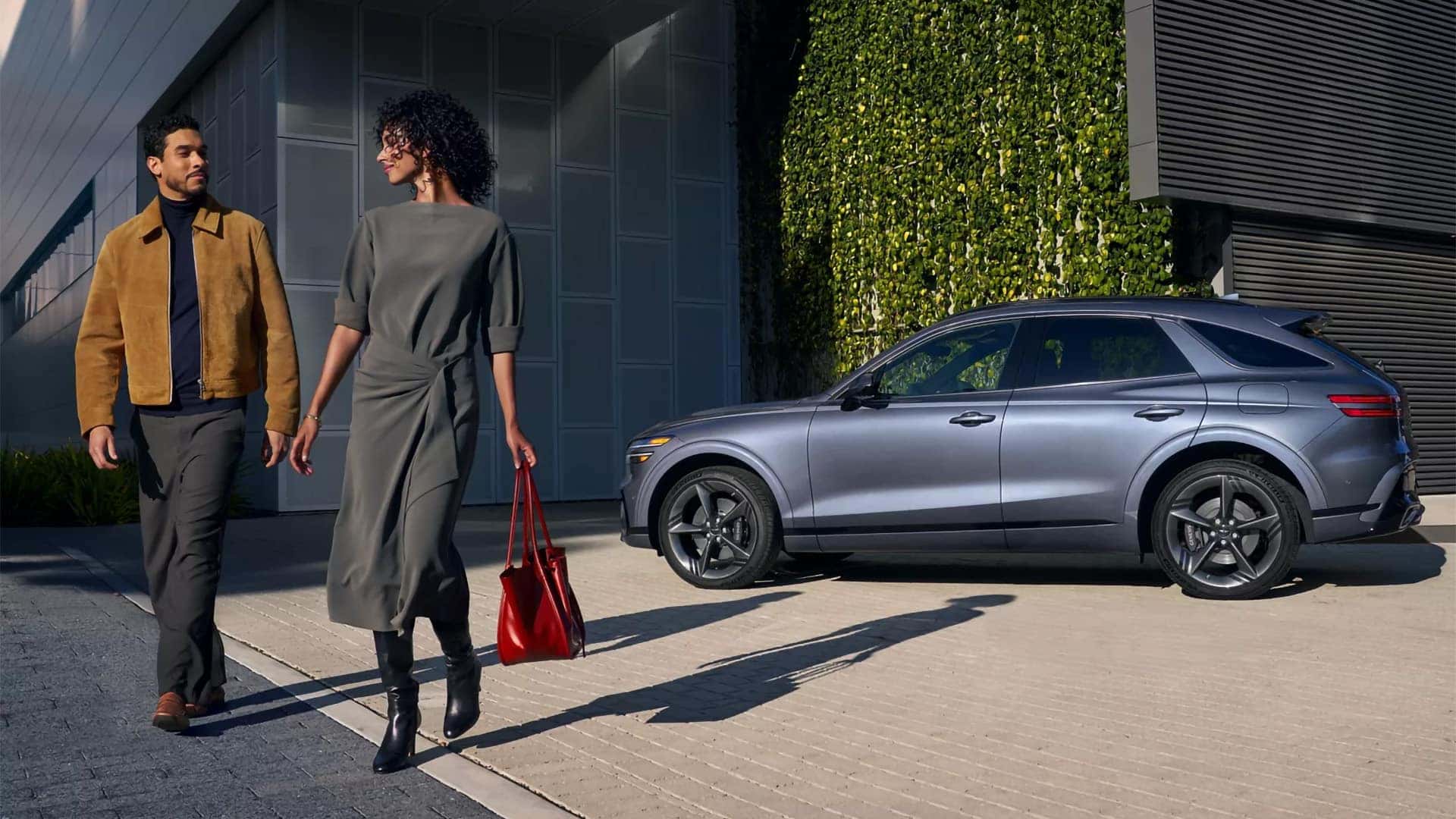 Two people walking past 2026 Genesis GV70 highlighting luxury SUV styling and available trim design details