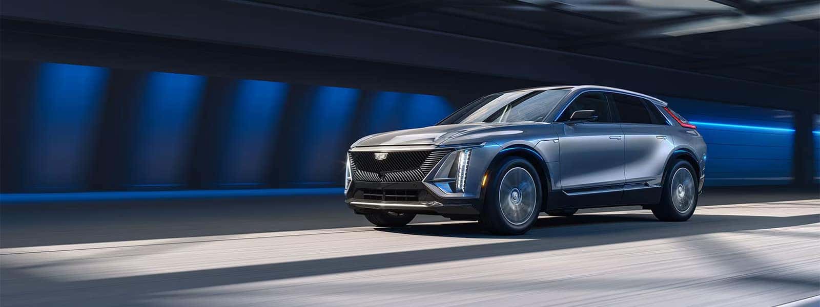 Silver 2026 Cadillac LYRIQ driving through a modern tunnel, showing the luxury electric SUV exterior, front grille, and LED lighting