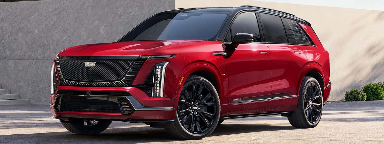 Red 2026 Cadillac VISTIQ luxury electric SUV shown from the front passenger side with black roof, vertical LED lighting, and black wheels