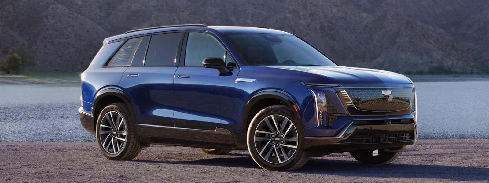 2026 Cadillac VISTIQ electric luxury SUV in blue parked by a lake with mountains in the background