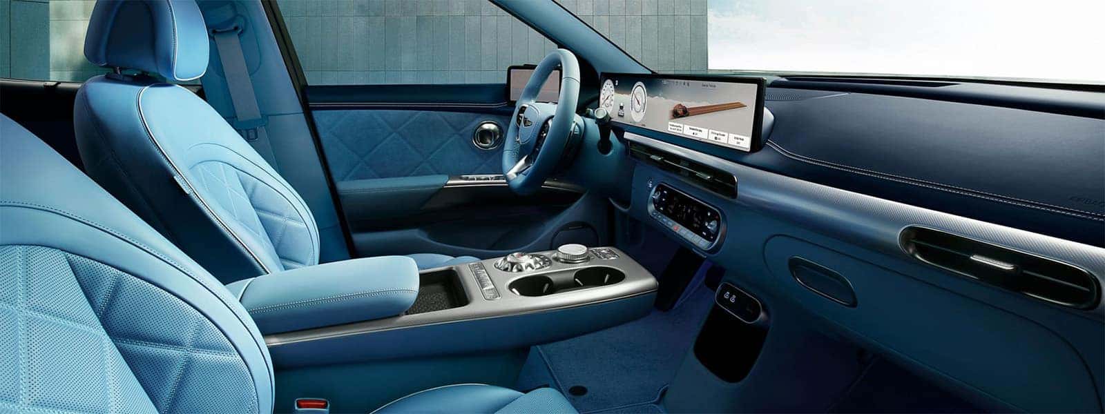 2026 Genesis GV60 interior with blue seating, wide digital display, center console controls, and premium electric SUV cabin design
