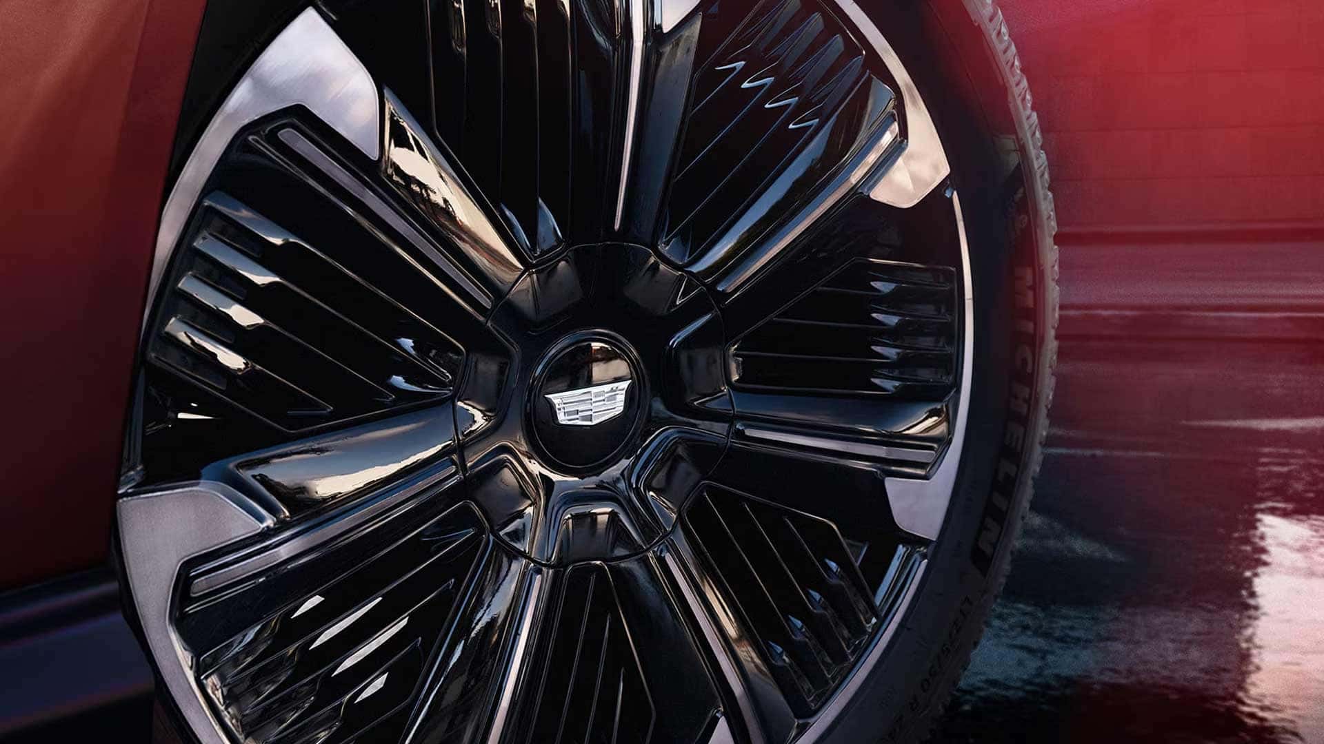 Close up of a Cadillac alloy wheel with black and silver multi spoke design and visible tire tread on wet pavement