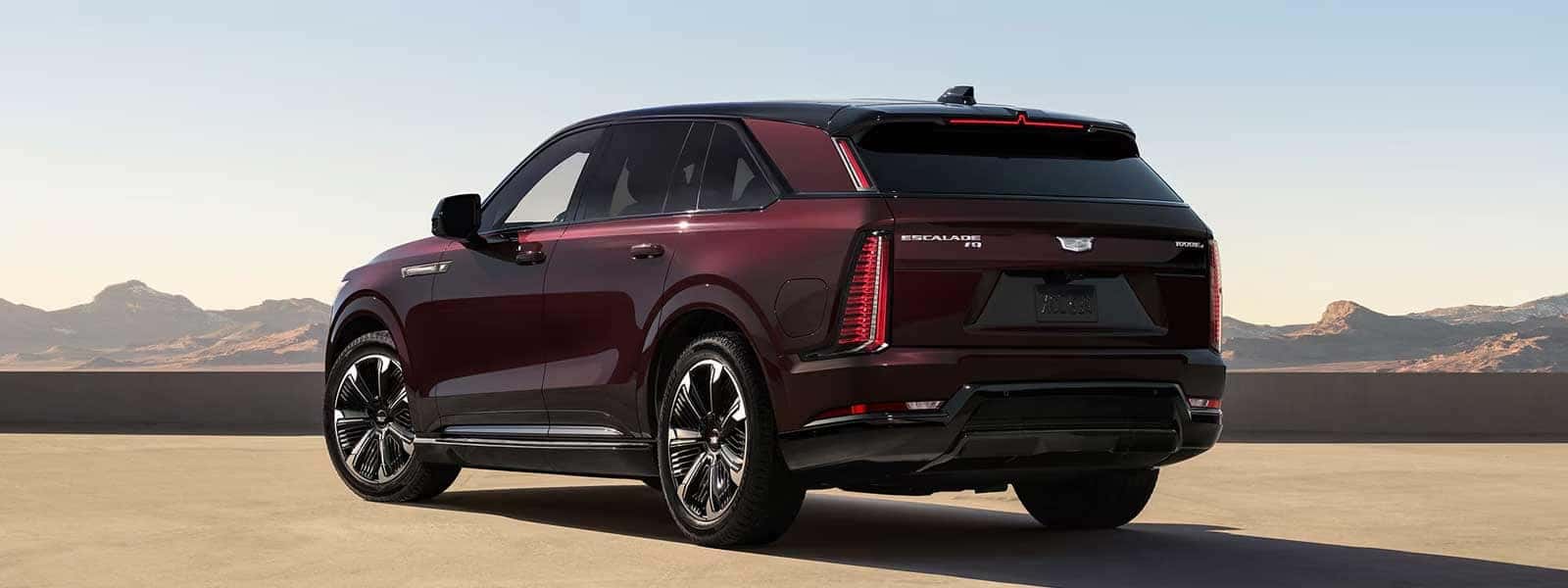 Rear three quarter view of a red Cadillac Escalade IQ parked outdoors with vertical taillights and mountains in background