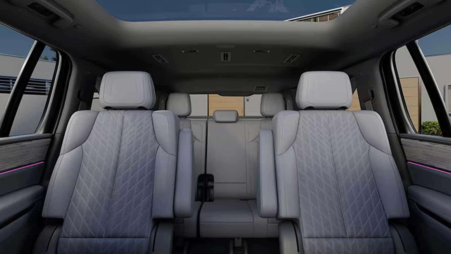 Interior view showing three rows of light-colored seats with quilted stitching and panoramic glass roof