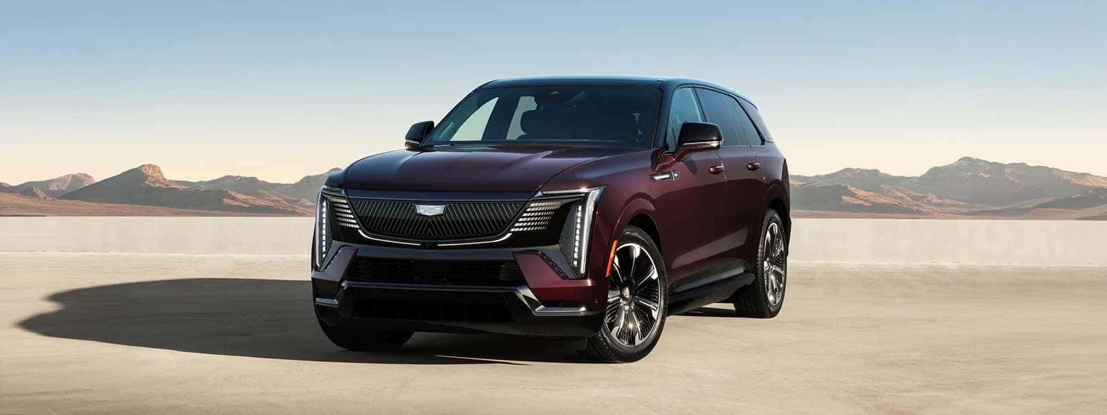 Red Cadillac Escalade IQ parked on a desert surface with mountains in the background under clear sky