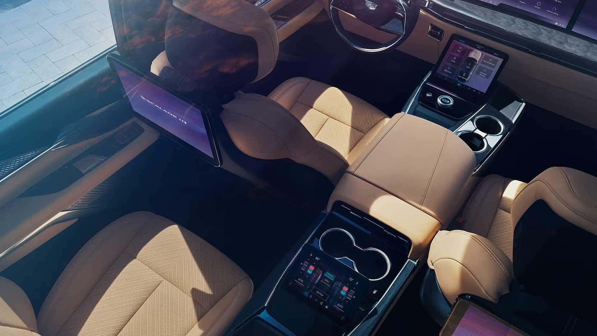 Overhead view of tan leather seats, center console, cupholders, rear screen, and dashboard controls