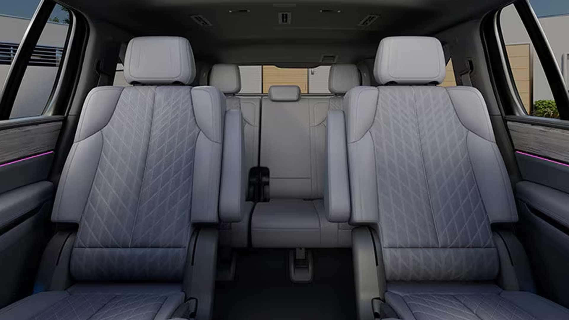 Second-row light leather captain's chairs with armrests, third-row bench, and pink ambient lighting
