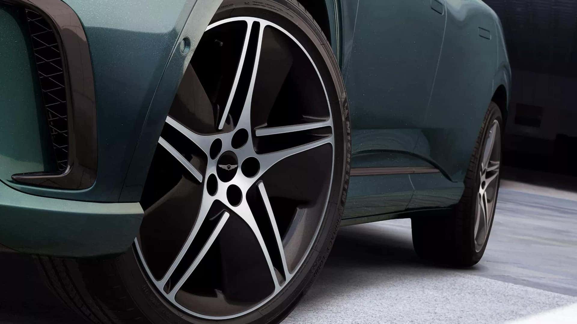 Close up of 2026 Genesis GV60 alloy wheel with five spoke design, front fender, and lower exterior trim detail