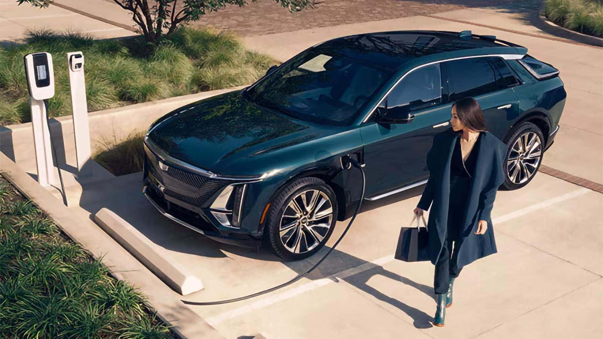 2026 Cadillac LYRIQ plugged into a public EV charging station with driver standing beside the electric SUV