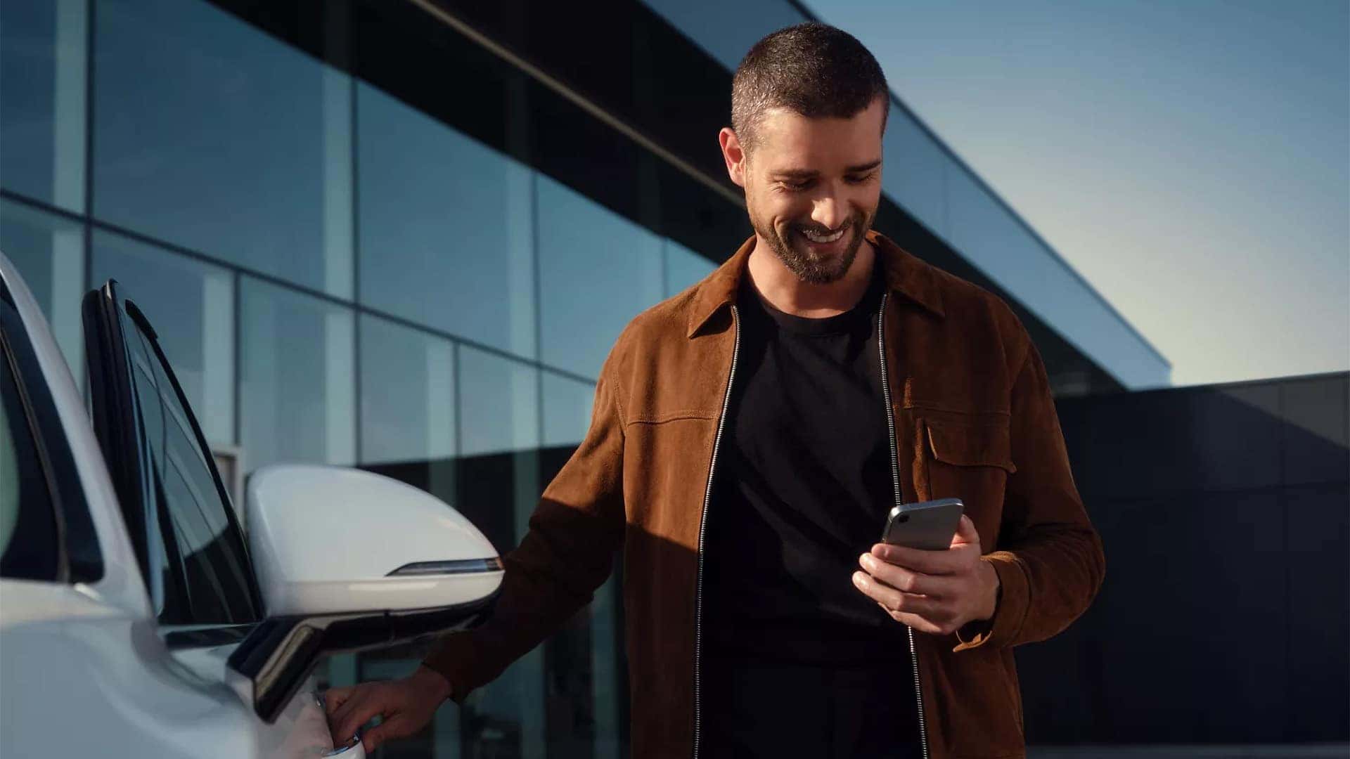 Driver using a smartphone beside the 2026 Genesis GV60 with connected services and digital key technology