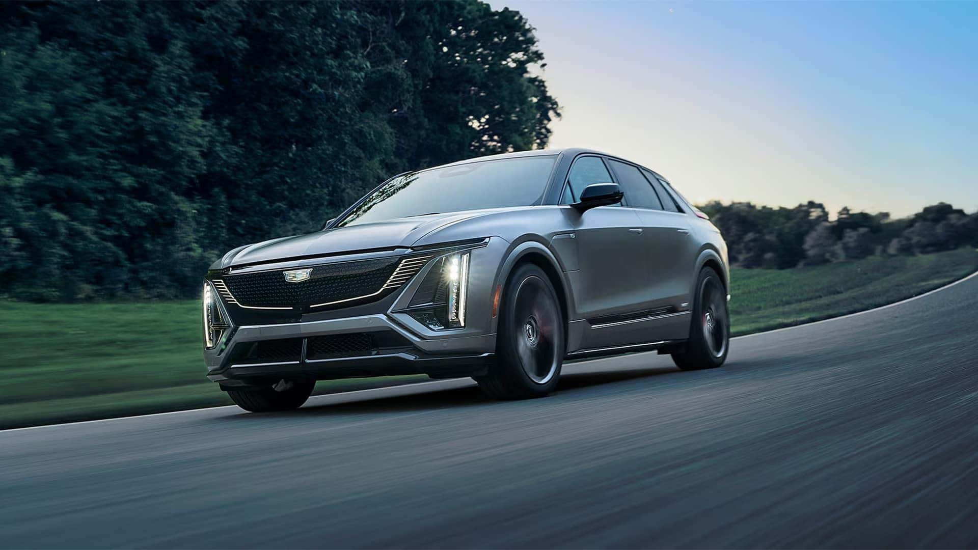 2026 Cadillac LYRIQ-V electric SUV driving on a curving road with sport styling and performance-focused exterior design