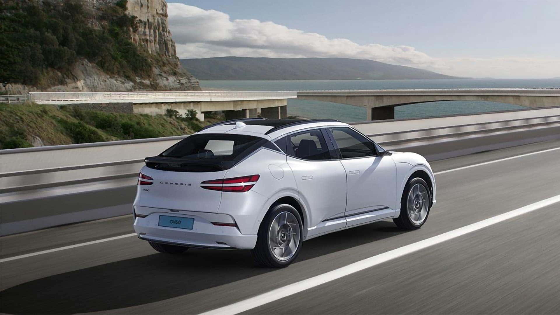 2026 Genesis GV60 electric luxury SUV driving on a coastal highway with rear exterior styling visible