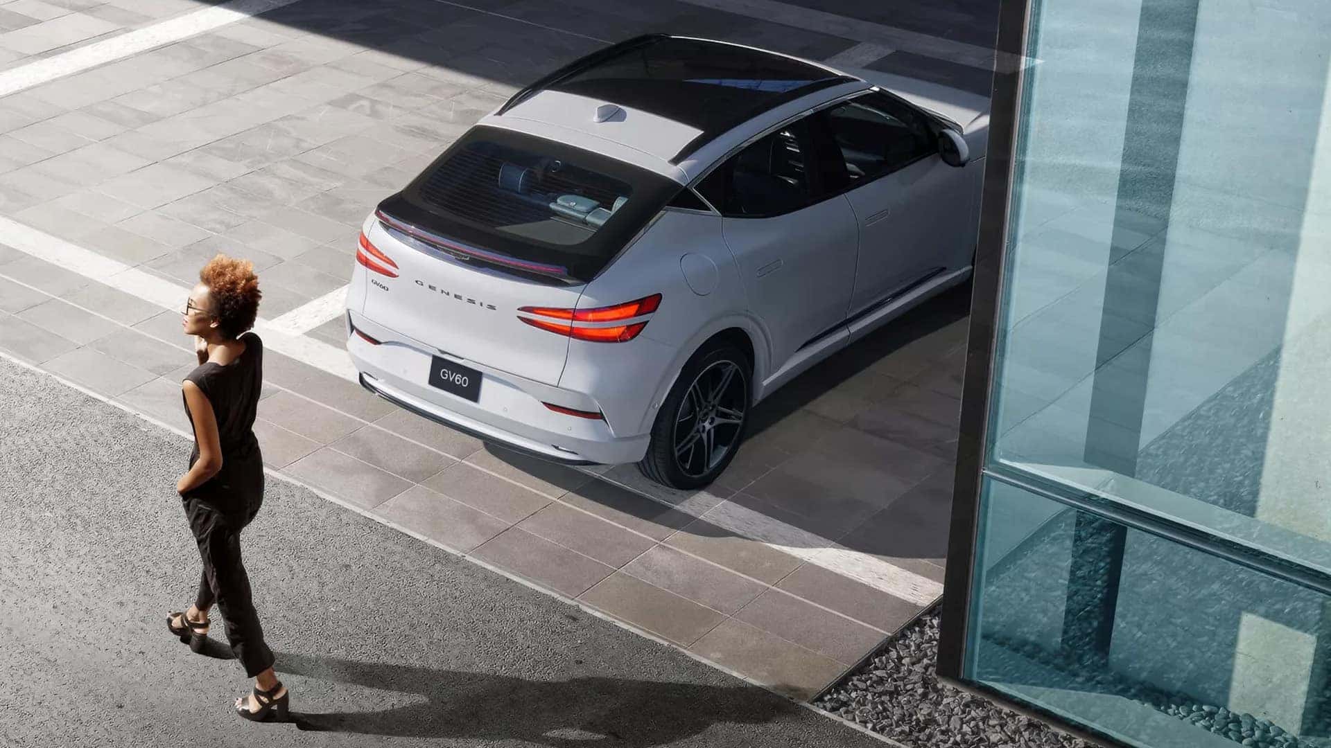 2026 Genesis GV60 parked near a modern building with smart parking assistance technology and exterior camera support