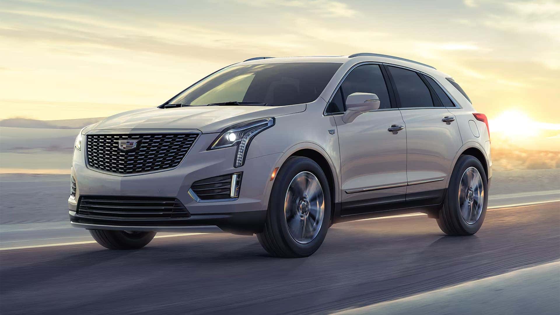 White 2026 Cadillac XT5 driving on an open road with Cadillac grille, LED headlights, and alloy wheels visible