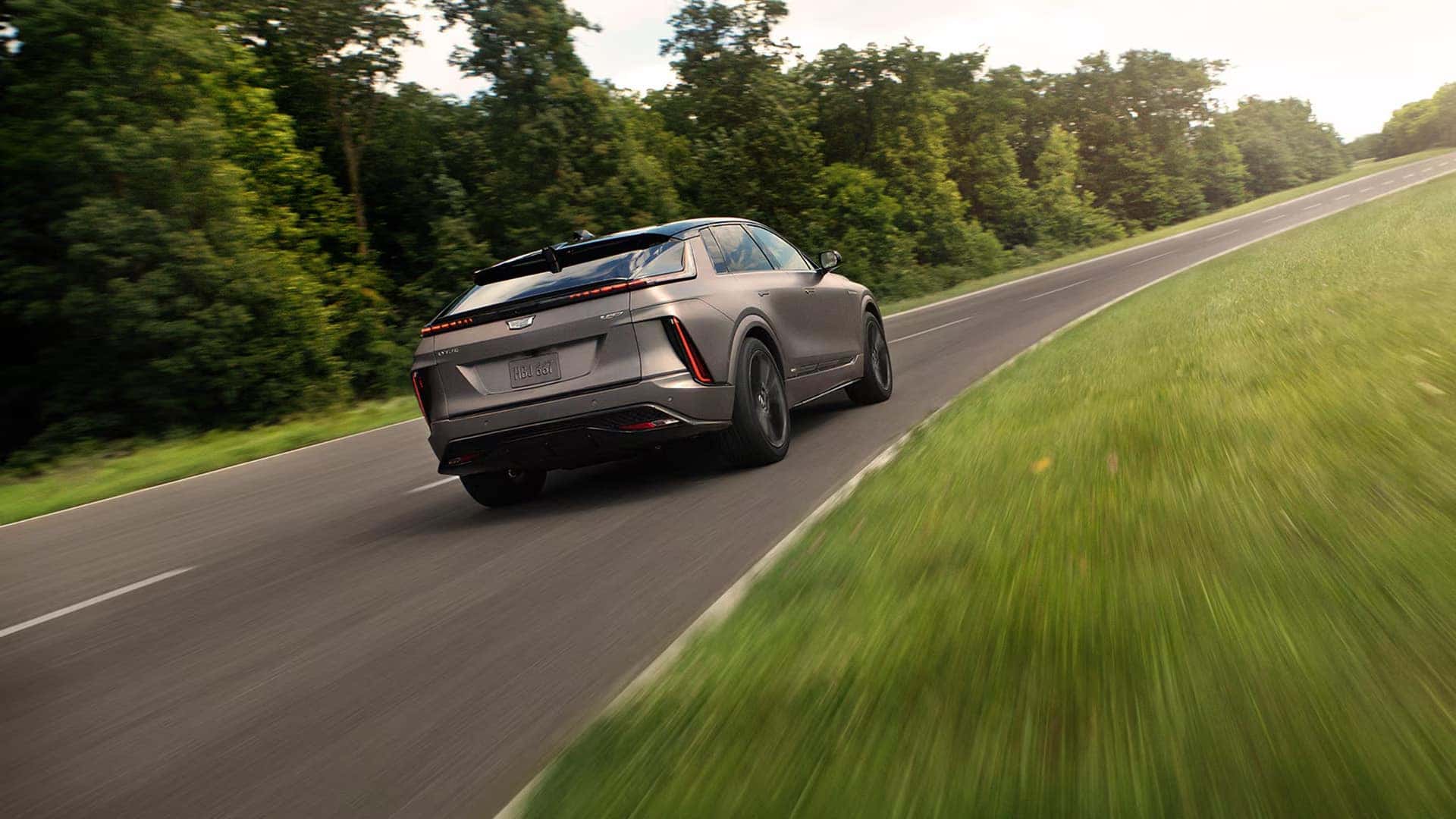 2026 Cadillac LYRIQ driving on a curving road, showing rear exterior styling, LED taillights, and luxury SUV proportions