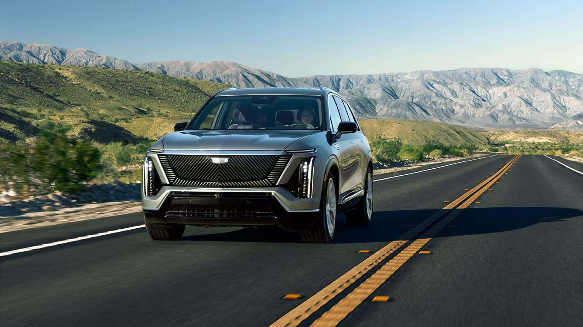 2026 Cadillac VISTIQ electric SUV driving on a mountain road, showing front LED lighting and luxury Cadillac styling