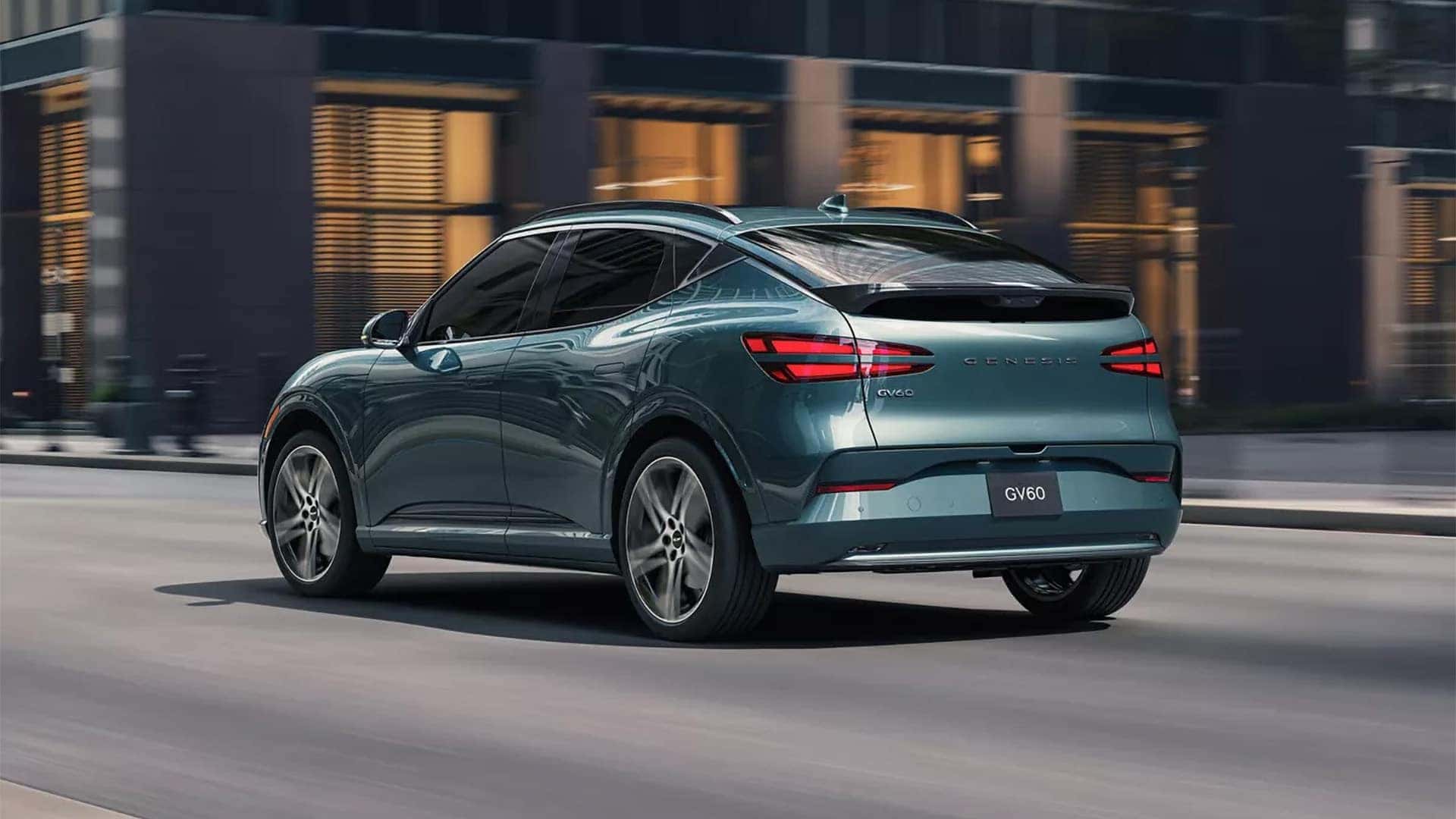 Rear three quarter view of 2026 Genesis GV60 driving through a city with LED taillights and premium exterior styling
