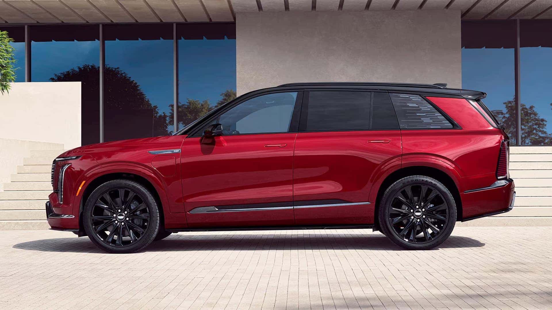 Side profile of a red 2026 Cadillac VISTIQ luxury electric SUV with black roof, black wheels, and long three row body design