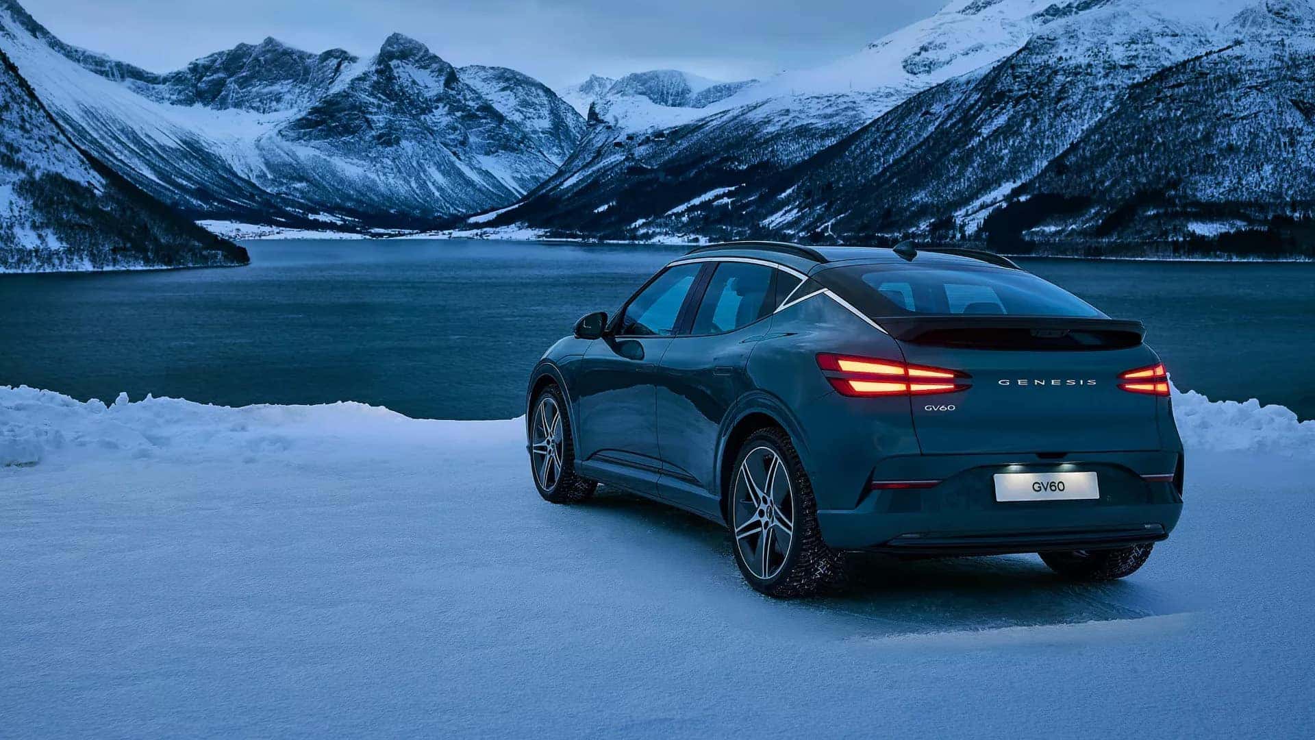 2026 Genesis GV60 parked near snowy mountains showing rear exterior design, LED taillights, and compact electric SUV proportions