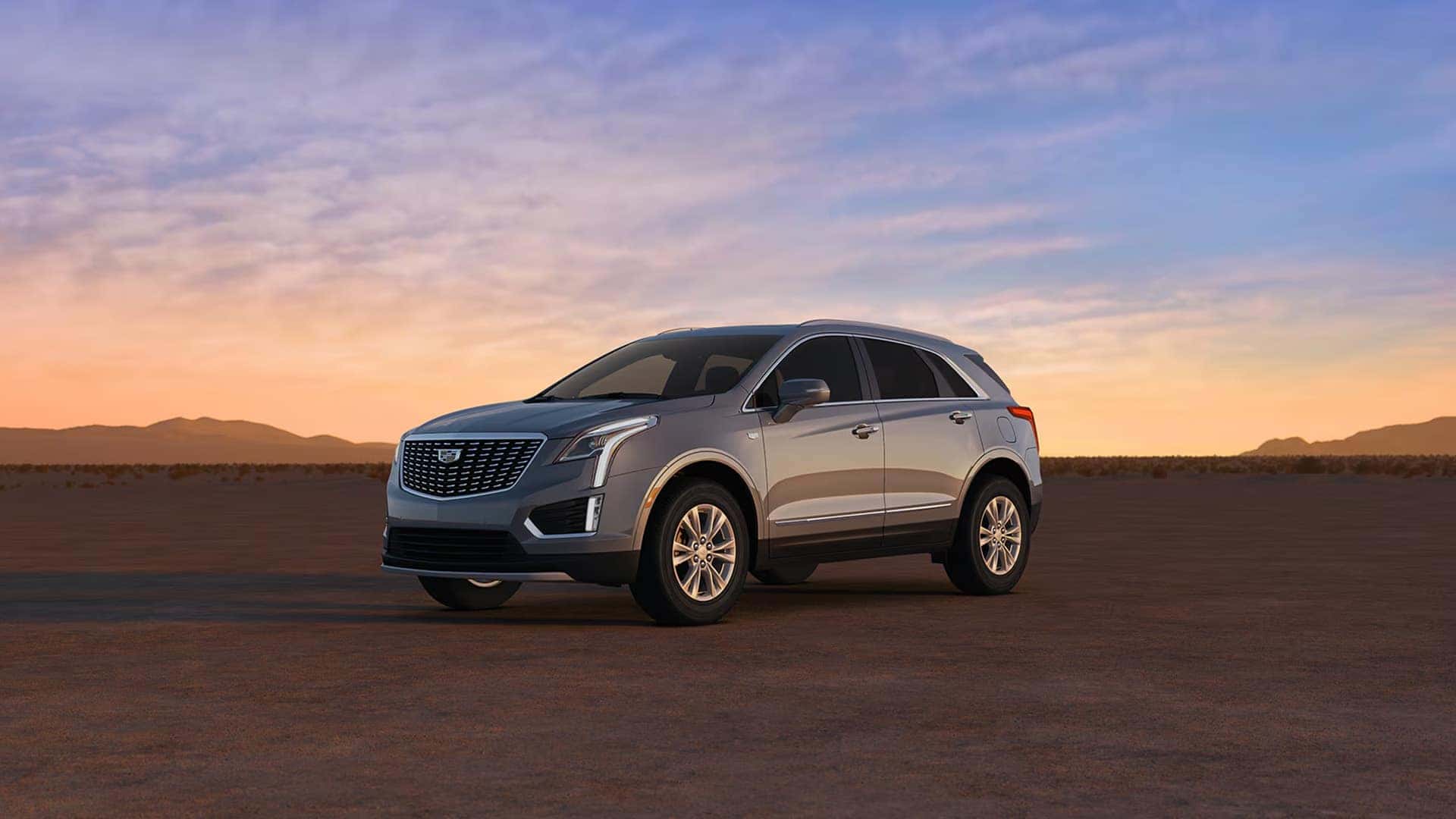 Silver 2026 Cadillac XT5 parked in desert landscape at sunset showing front grille, wheels, and exterior proportions
