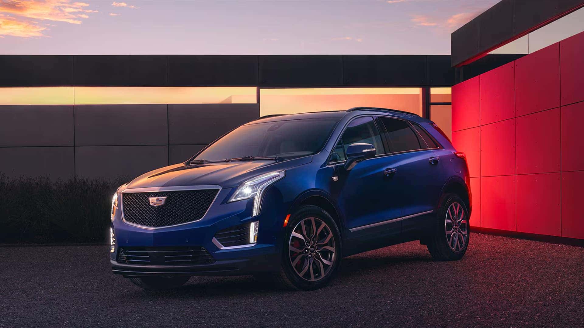 Blue 2026 Cadillac XT5 parked near a modern building with front grille, LED lighting, and alloy wheels visible
