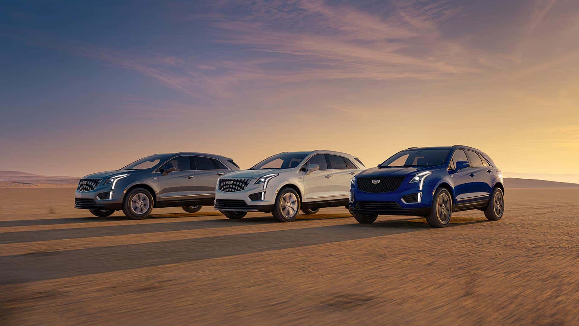 Three 2026 Cadillac XT5 SUVs driving across a desert landscape showing multiple exterior colors and trim styles